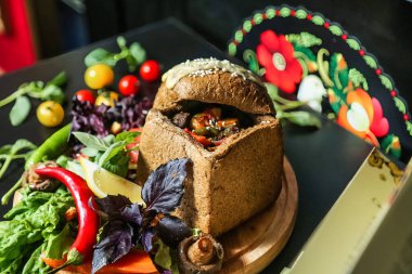 Tahta tabağa lezzetli bir sandviç konur ve rengarenk taze sebzelerin yanına yerleştirilir..