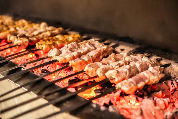 stock image A BBQ grill is cooking a variety of meat and vegetables, creating a delicious and savory meal.