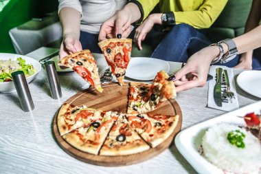 Birkaç kişi bir masanın etrafında toplanmış, birlikte pizza yiyor ve eğleniyorlardı..