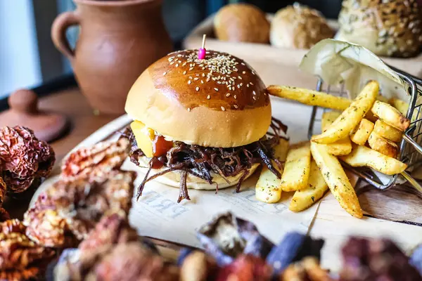 stock image A mouth-watering hamburger and a portion of crispy french fries are placed on a wooden cutting board.