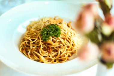 Beyaz bir tabak spagetti ile kaplıdır ve üzeri canlı yeşil brokoli çiçekleriyle kaplıdır..