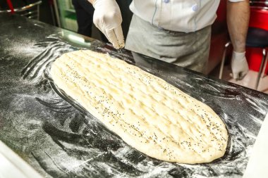 Beyaz eldiven giyen biri pizza hazırlar, malzemeleri birleştirir ve hamuru şekillendirir..