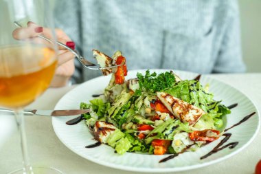 Çatalla salata yerken masada oturan bir kadın..