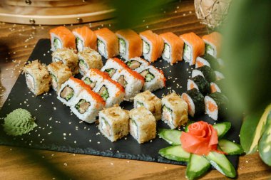 Siyah bir tabak taze suşi ruloları ve dilimlenmiş salatalıkla süslenir..