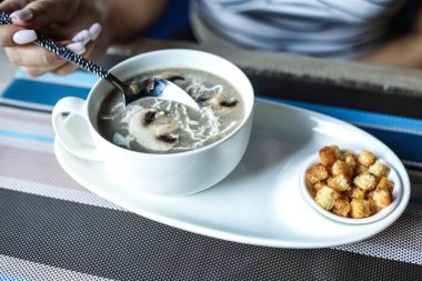 Bir kişi bir kase çorbanın içinde kaşık tutarken görülüyor..