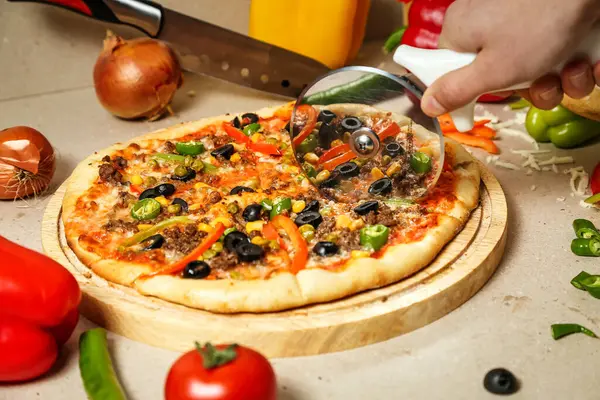 Yeni pişmiş pizzayı dilimlemek için pizza kesicisi kullanan biri..