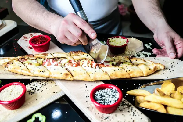 Bir insan ustalıkla tahta kesme tahtasıyla pizza kesiyor..