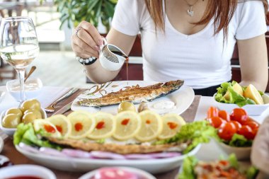Bir kadın masada oturuyor, önünde lezzetli bir tabakla yemeğin tadını çıkarıyor..