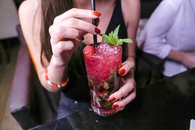 Bir kadın bir elinde taze toplanmış çilek bir elinde taze bir içecek tutar..