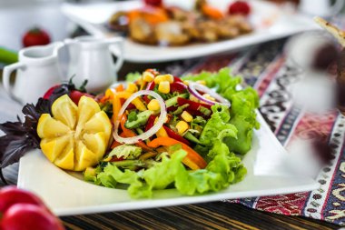 Taze salatayla birlikte beyaz bir tabak, yanında da güzel yemekler, düzgünce bir masaya dizilmiş..