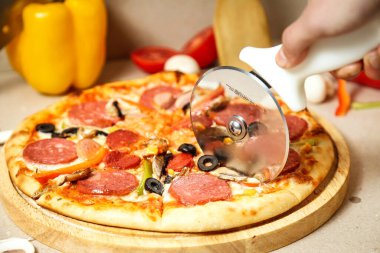 Pizza kesicisiyle büyük bir dilim pizza kesen bir elin yakın plan fotoğrafı..