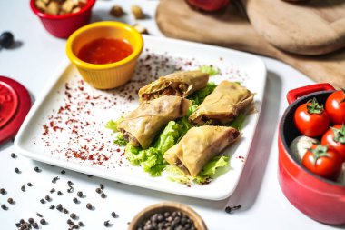 Lezzetli bir yemek çeşidiyle kaplı beyaz bir tabak lezzetli sosla dolu bir kasenin yanında oturur..