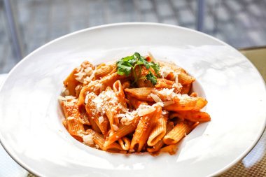 Zengin domates sosuyla kaplı ve rendelenmiş parmesan peyniri serpiştirilmiş bir tabak makarna..