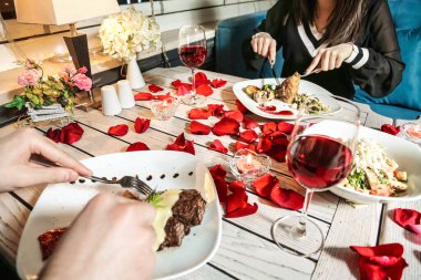 Bir grup birey masada oturuyor, sohbet ediyorlar ve yemeklerini yiyorlar..