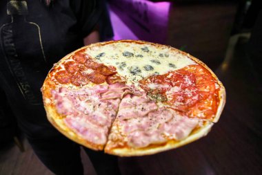 Bir insan ağız sulandırıcı malzemelerle dolu bol soslu bir pizza tutar..