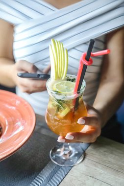 Bir kadın cep telefonu ekranına dikkatle bakarken elinde bir içki tutuyor..