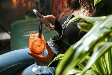 Bir kadın cep telefonuyla koltukta otururken görülüyor..