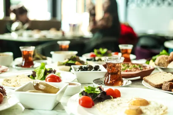 Tabaklar dolusu yemek ve fincanlar da dahil olmak üzere çeşitli yemek ve içecekler bir masaya dizilmiştir..