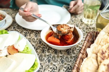 Bir insan masaya oturmuş çatal ve bıçakla yemek yiyor..