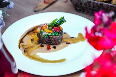 Beyaz bir tabak, bol sosla kaplı bir parça etle sunulur..