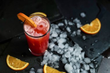 Canlı kırmızı bir içecek, turuncu bir garnitür ve buz ile canlandırıcı bir içecek..
