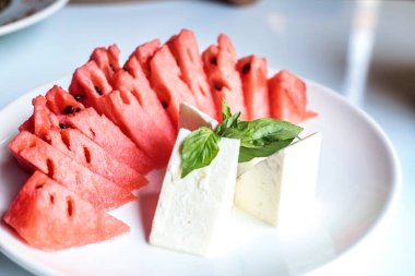 Beyaz tabakta sulu karpuz ve krem peynir dilimleri var..