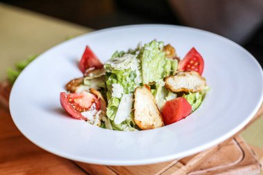 Çeşitli karışık yeşilliklerden yapılmış canlı bir salatanın yakın plan görüntüsü, ahşap bir masanın üzerine yerleştirilmiş beyaz bir tabakta dinleniyor..