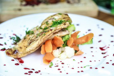 Beyaz bir tabak lezzetli, nemli et ve renkli taze sebzelerle doludur..