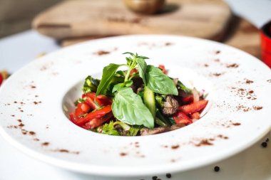 Beyaz tabakta taze marul ve sulu domateslerle kaplı bir salata var..