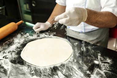 Beyaz eldiven giyen bir adam ustalıkla çeşitli malzemelerle bir pizza hazırlar..