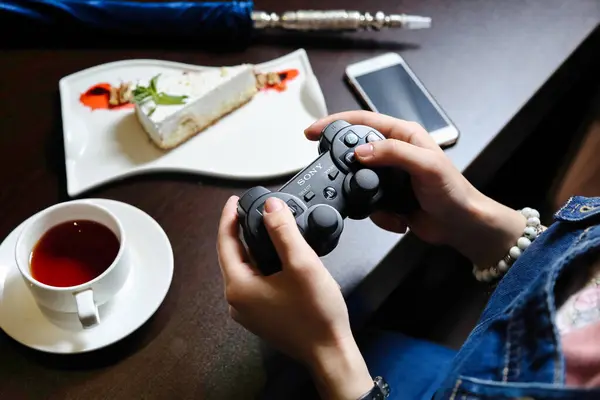 Bir kişi bir fincan çayın yanında otururken bir video oyun kumandası tutar..