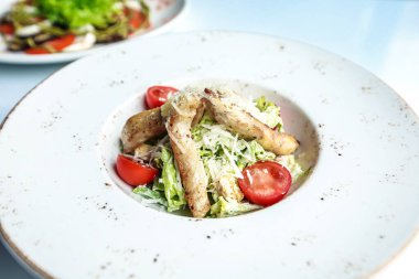 Beyaz bir tabak renkli bir salata ile doldurulur ve üstü kızarmış tavukla kaplanır..