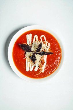 Erimiş peynirle kaplı sıcak domates çorbası dolu bir kase..