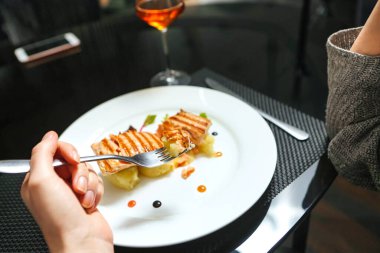 Beyaz bir tabak lezzetli yiyeceklerle süslenir ve bir kadeh şarabın yanına yerleştirilir..