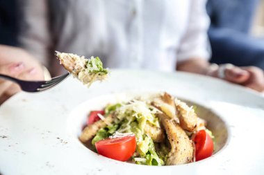 Restoran masasında oturan bir insan taze ve besleyici bir salata yemek için çatal kullanır..