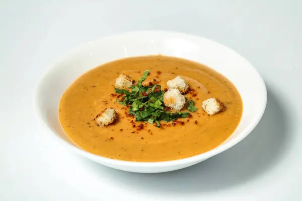 Lezzetli çorbayla dolu beyaz bir kase ve üstü çıtır kıtır ekmek..