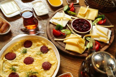 Lezzetli bir omlet, sosis, çeşitli peynir, meyve ve bir fincan koyu Türk çayı içeren geleneksel bir Türk kahvaltısı..