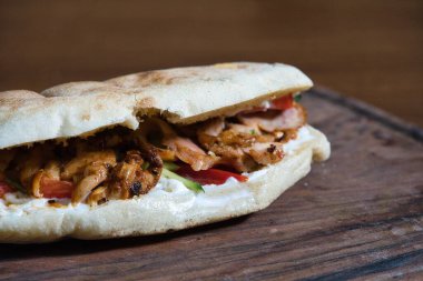 Sebzeli ve kremalı tavuklu shawarma sandviçi. Yumuşak pide soslu. Tahta tahtada servis ediliyor..