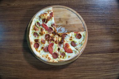 Biberli, domatesli ve yeşil biberli, altı parçaya bölünmüş, ahşap bir masada yakın plan bir pizza..