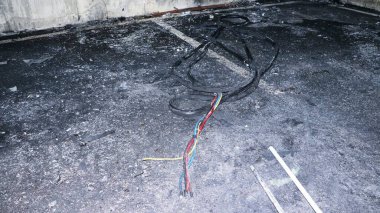 Beton bir zeminde yanmış kablolar ve enkazın yakın çekim görüntüsü, muhtemelen yangından sonra..