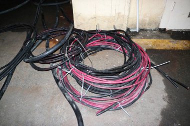 Beton zeminde siyah ve kırmızı elektrik kablolarının karışıklığı duruyor..