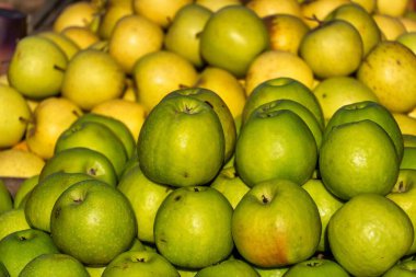 Bir pazarda sergilenen yeşil ve sarı elmaların yakın plan görüntüsü.