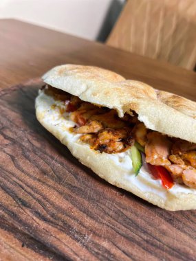 Beyaz soslu, marullu ve domatesli tavuklu shawarma sandviçi ahşap bir kesim tahtasının üzerinde..