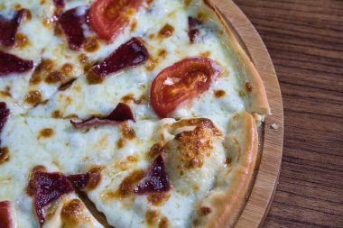 Erimiş peynir, domates dilimleri ve ahşap bir tahtanın üzerinde et olan bir pizzanın yakın plan görüntüsü..