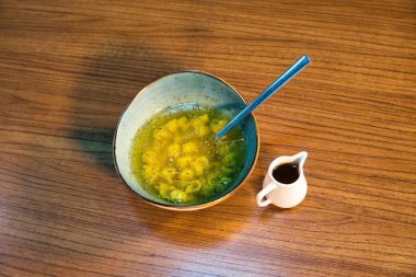 Bir kase sarı makarna yeşil otlar ve ahşap bir masada sos, yanında da küçük bir sürahi sos..