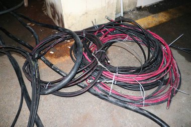 Bir yığın siyah ve kırmızı elektrik kablosu beton zeminde duruyor..