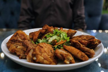 Kızarmış tavuk parçaları ve salata bir restoran ortamında beyaz bir tabakta düzenlenir..