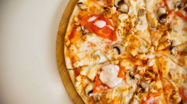 Tavuklu, mantarlı ve peynirli bir pizza. Pizza ahşap bir tahtanın üzerinde ve kısmen dilimlenmiş..