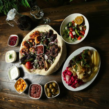 Ahşap bir masada çeşitli garnitürlerle büyük bir tabakta çeşitli ızgara et ve sebzeler servis edilir..