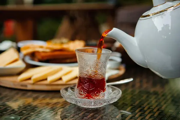 Beyaz bir çaydanlık, açık bir kafede geleneksel bir bardağa sıcak çay doldurur..